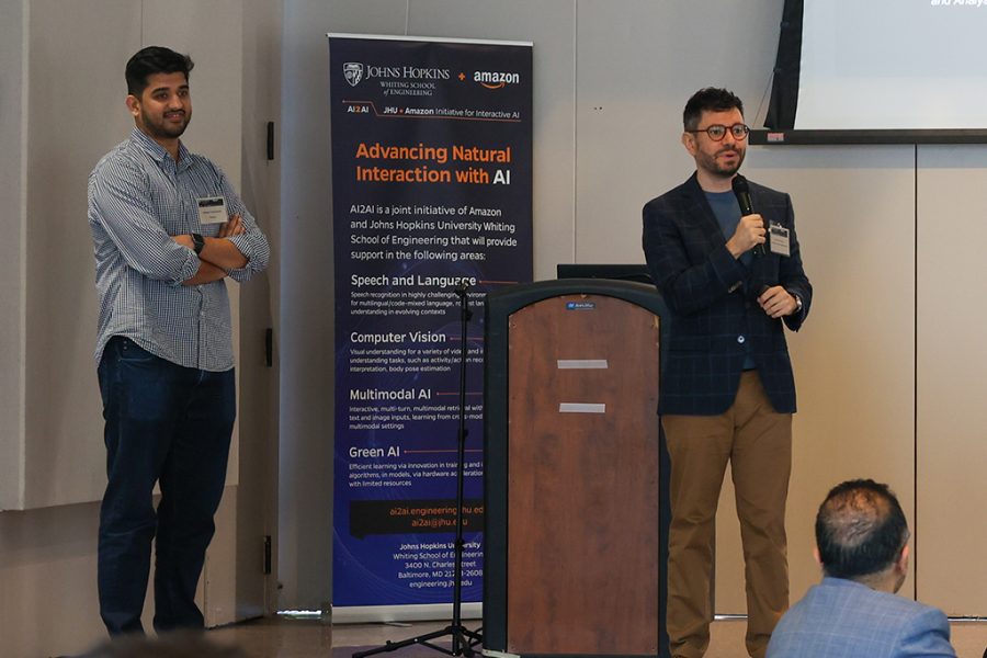 Venkatesh (Venky) Ravinchandran, Applied Science Manager, Alexa, stands onstage beside Laureano Moro Velazquez (right), 2022-2023 AI2AI Research Award PI, who is presenting work completed towards his awarded research project