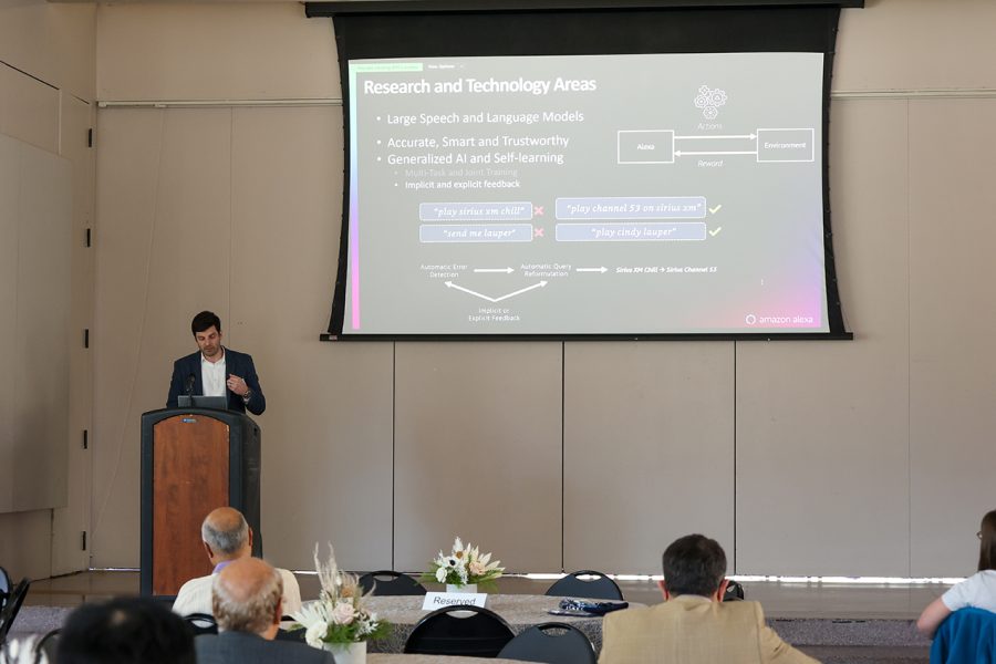 Grant Strimel, Principal Scientist, Amazon Alexa, stands at a podium onstage to present the Alexa team's overview and topics of interest