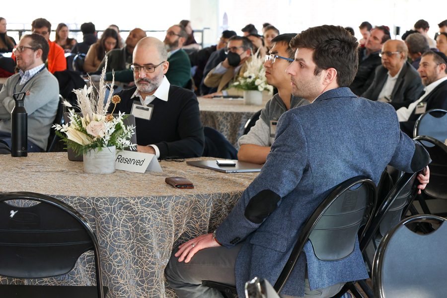 Vincent Ponzo, Amazon; Jing Liu, Senior Applied Scientist, Alexa AI; and Grant Strimel, Principal Scientist, Alexa, sit at a round table while observing the presentation occurring on stage to their left.
