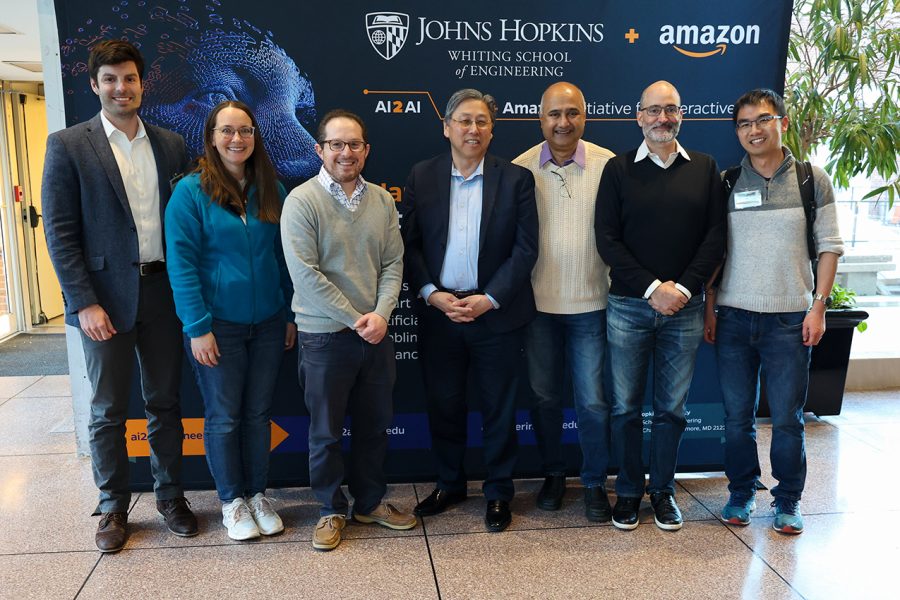 Grant Strimel (Amazon), Kelly Rooker (Amazon), Seth Zonies (JHU), Larry Nagahara (JHU), Sanjeev Khudanpur (JHU), Vince Ponzo (Amazon), and Jing Liu (Amazon) pose in front of an AI2AI banner