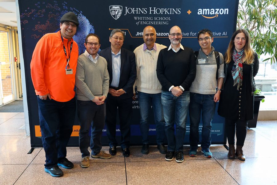 Najim Dehak (JHU), Seth Zonies (JHU), Larry Nagahara (JHU), Sanjeev Khudanpur (JHU), Vince Ponzo (Amazon), Jing Liu (Amazon), and Soledad Villar (JHU) pose in front of an AI2AI banner